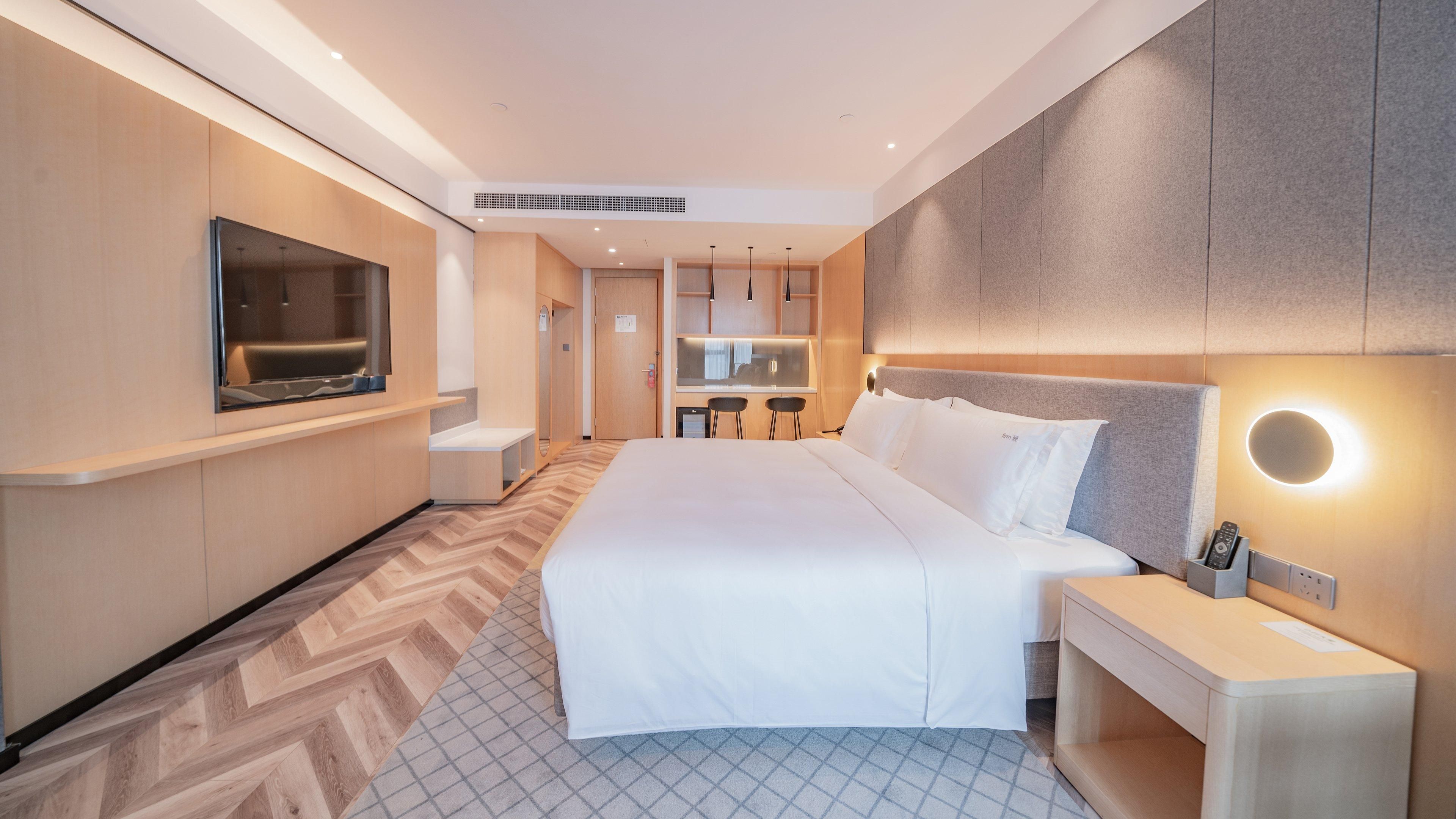Una habitación de hotel moderna con una cama grande, televisor, escritorio y espejo.