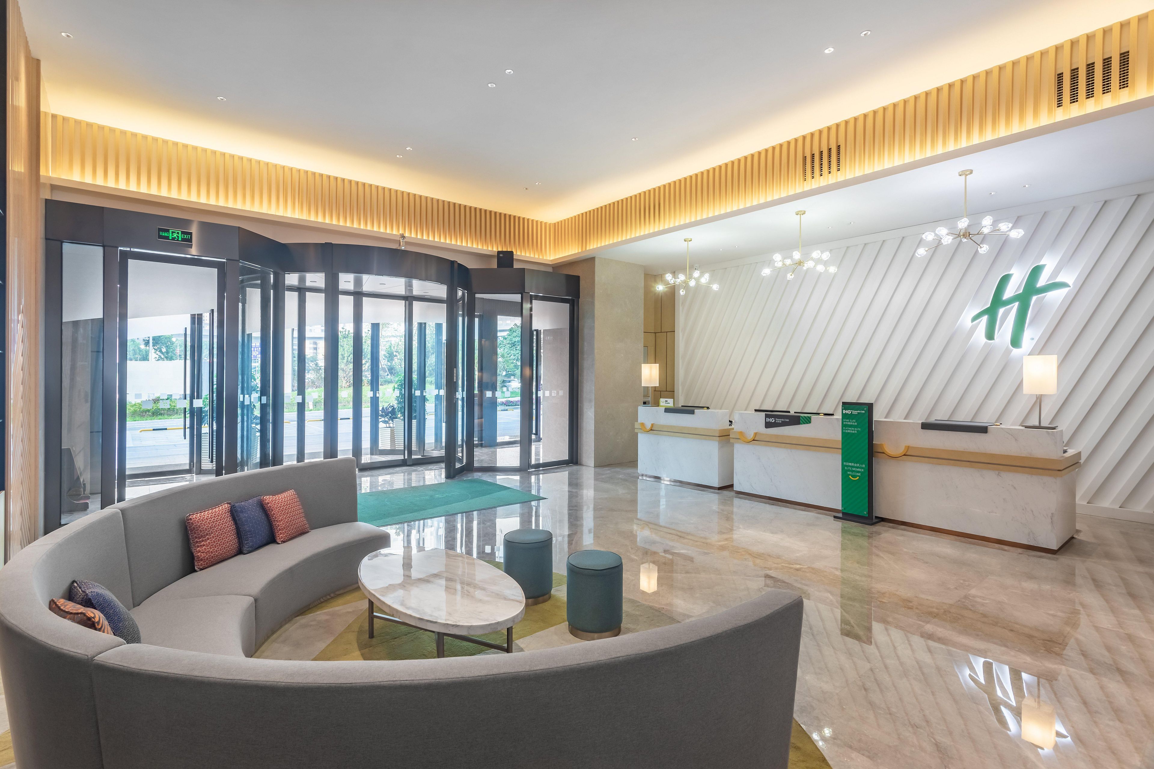 A modern lobby with a reception desk, a curved seating area, and a large window offering a view of the outdoors.