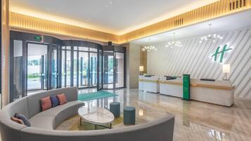 A modern lobby with a reception desk, a curved seating area, and a large window offering a view of the outdoors.