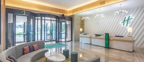 A modern lobby with a reception desk, a curved seating area, and a large window offering a view of the outdoors.