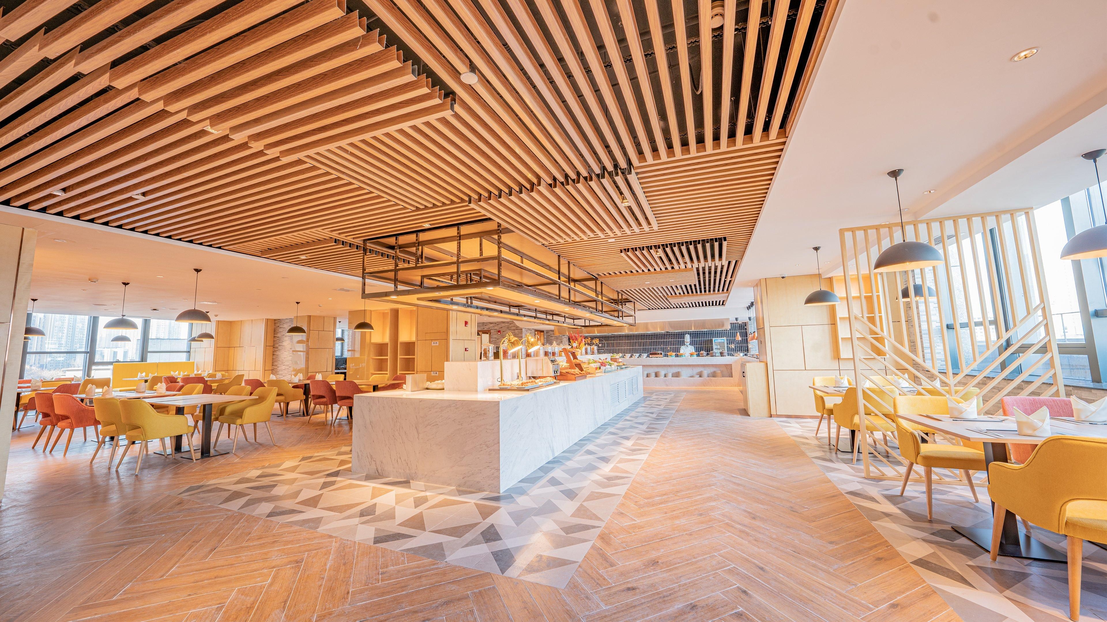 A spacious hotel lobby with a central bar area, multiple seating arrangements, and a modern ceiling design.
