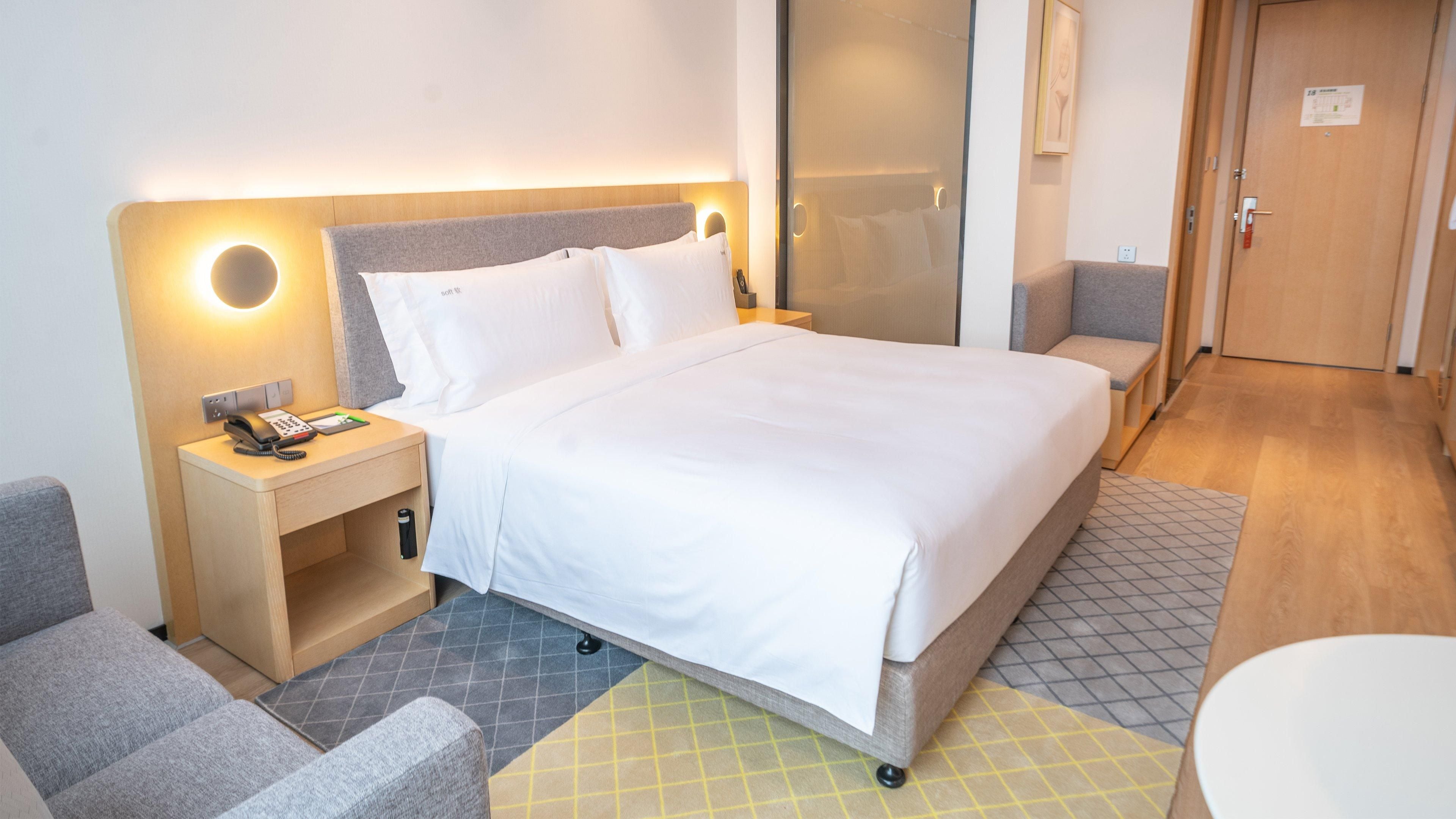 Ein Hotelzimmer mit Bett, Nachttisch mit Telefon, einem Sessel, einem kleinen Tisch und einer Tür.