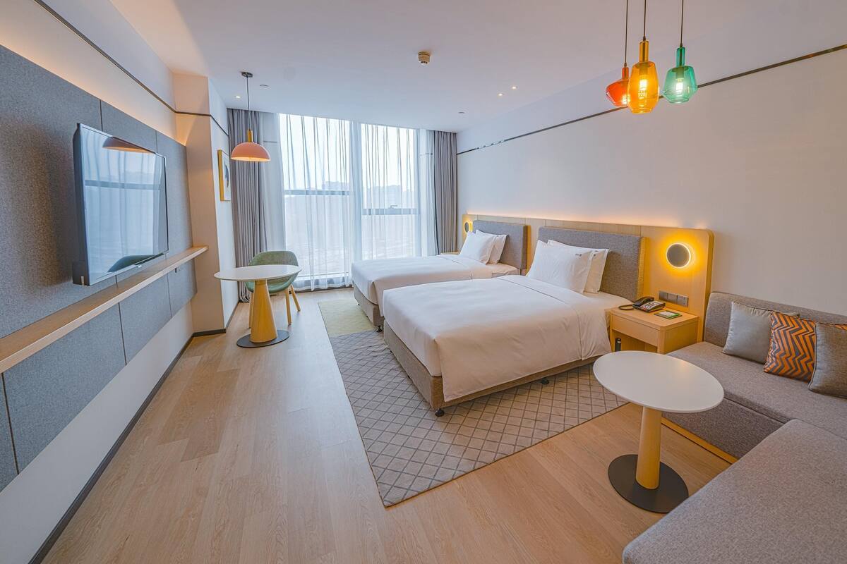 A modern hotel room with two beds, a sofa, a small table, and a TV.