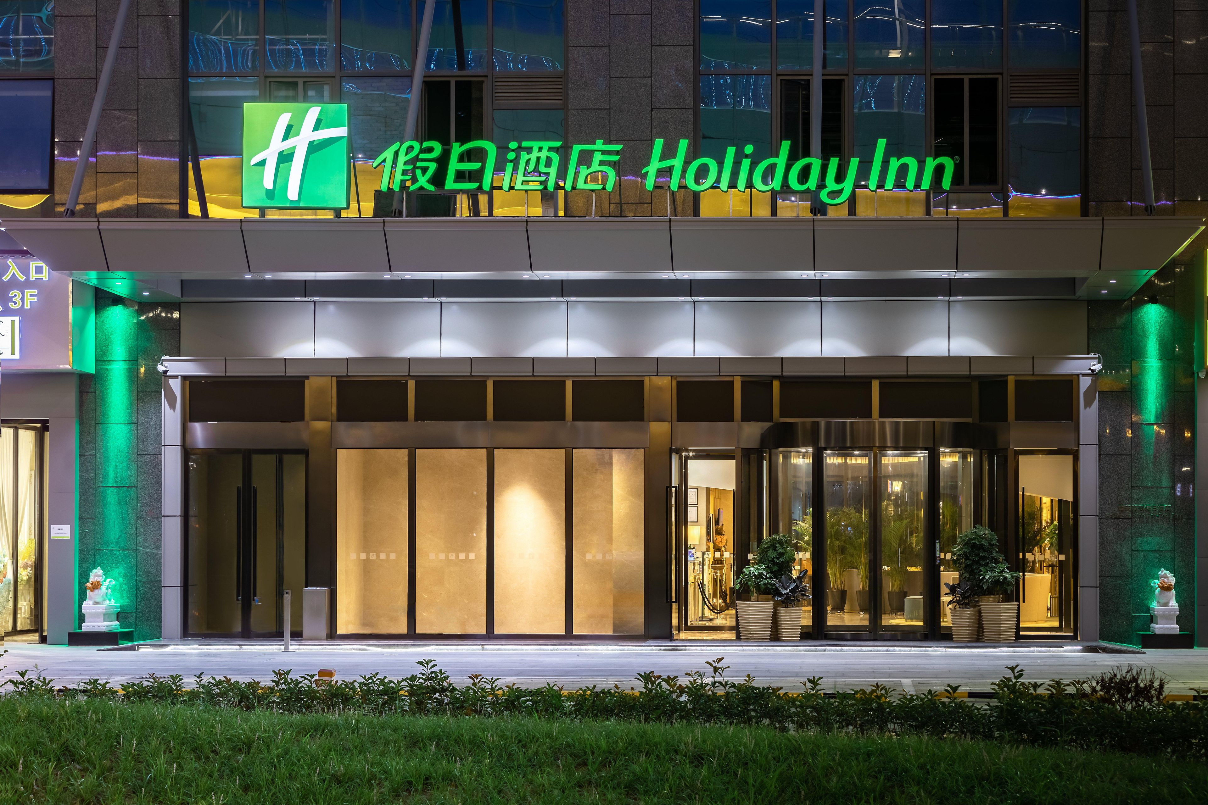 A Holiday Inn hotel entrance with a large illuminated sign, glass doors, and a well-lit facade.