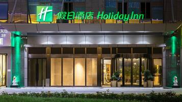 A Holiday Inn hotel entrance with a large illuminated sign, glass doors, and a well-lit facade.