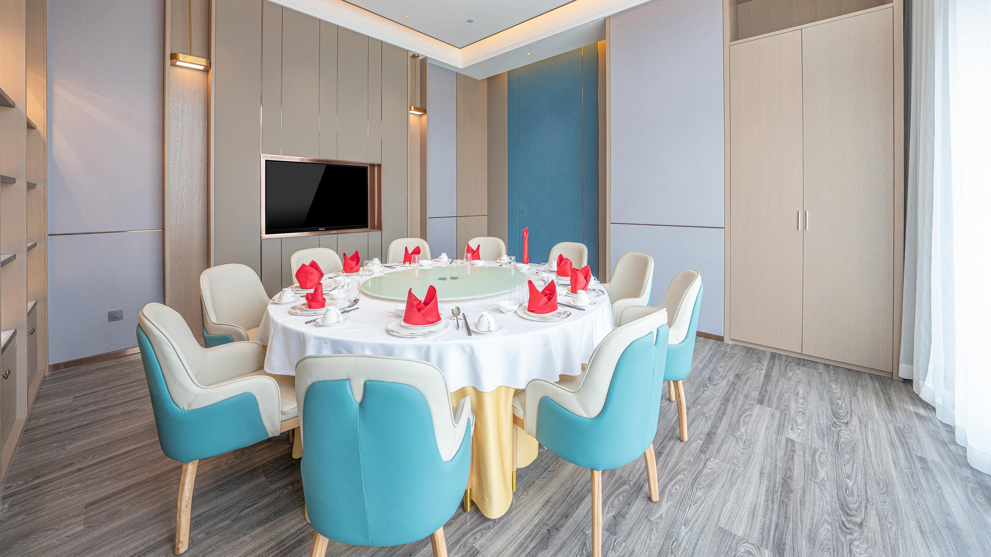 A conference room with a round table, chairs, a flat-screen TV, and a large cabinet.