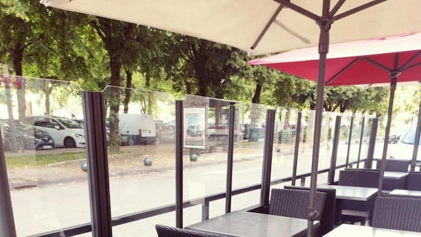 An outdoor seating area with tables and chairs, large windows, and a red umbrella. - Hôtel du Parc, Rte Le Rouget de Lisle (Lons-le-Saunier)