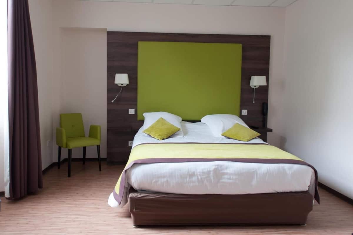 Una habitación de hotel con una cama, un sillón verde y un cabecero de madera.
