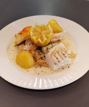 Un plato de comida con pescado, patatas y una guarnición de limón.