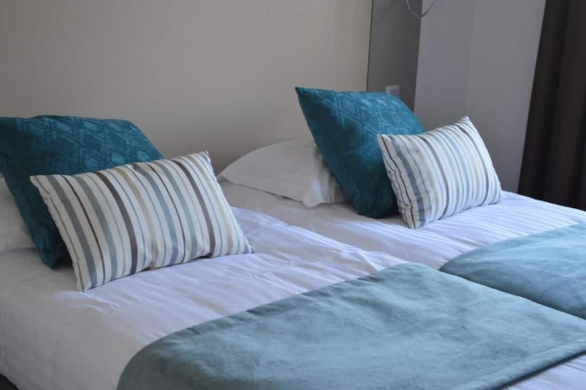 Una cama con ropa blanca, almohadas color turquesa y un cojín a rayas.