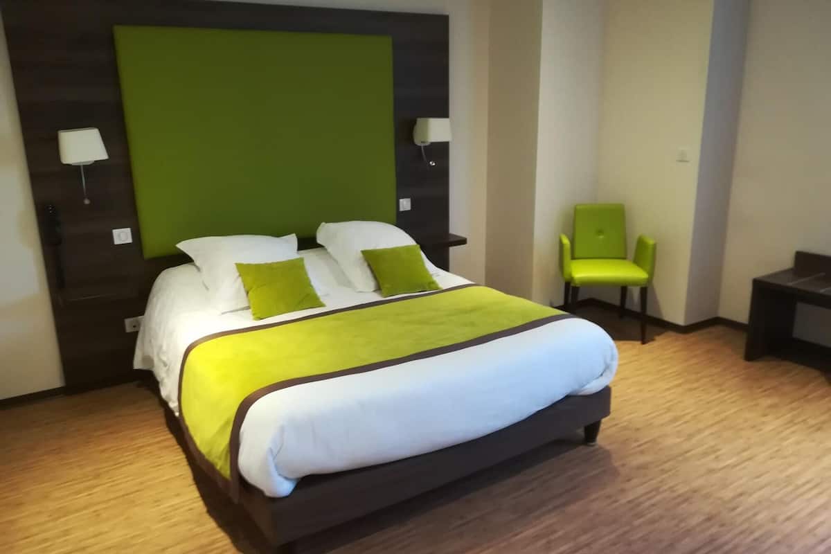 Habitación de hotel con una cama grande, un muro decorativo verde, una sola silla y una mesita pequeña.