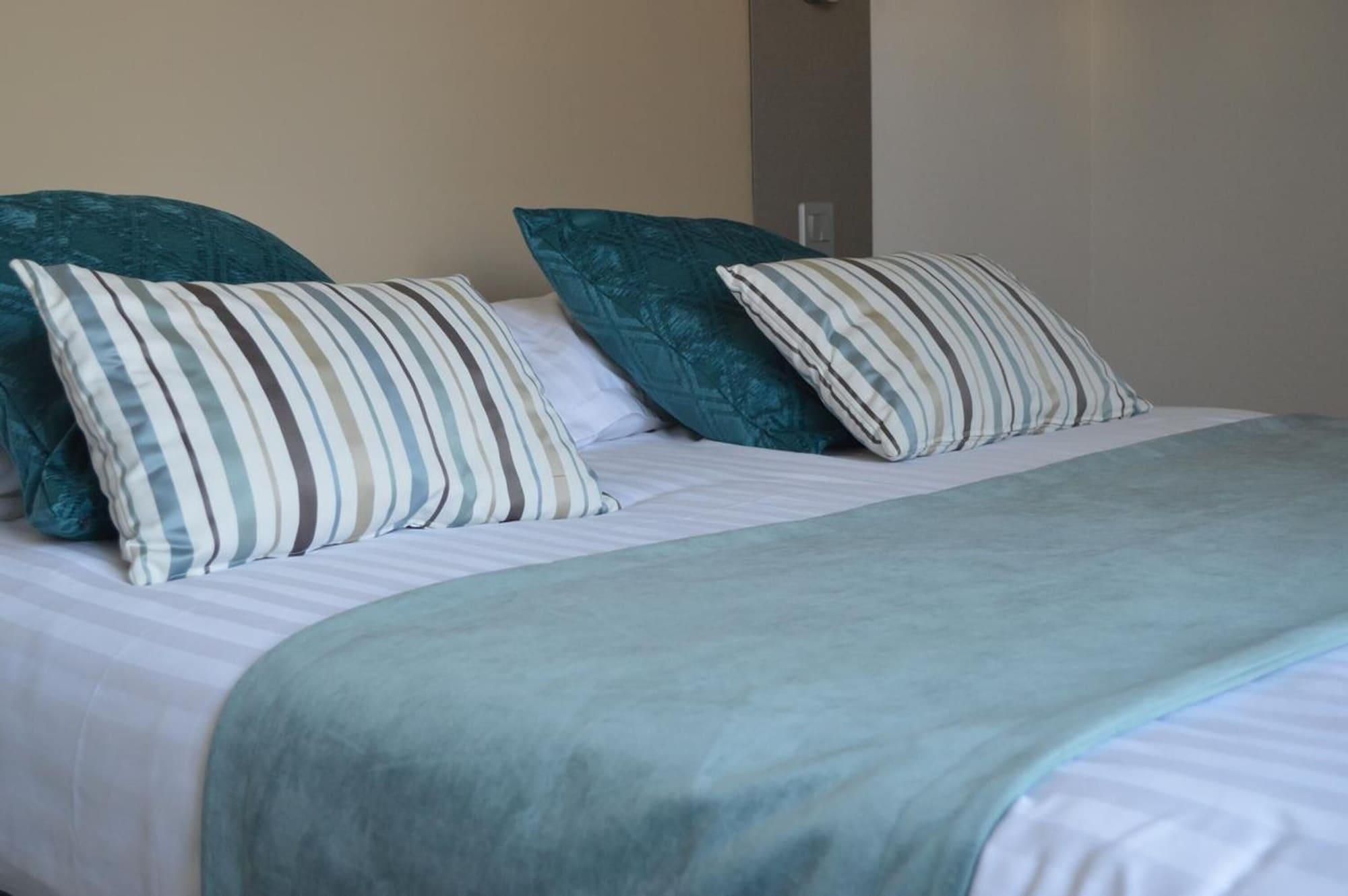 Un lit avec des oreillers à rayures et une couverture de couleur turquoise.