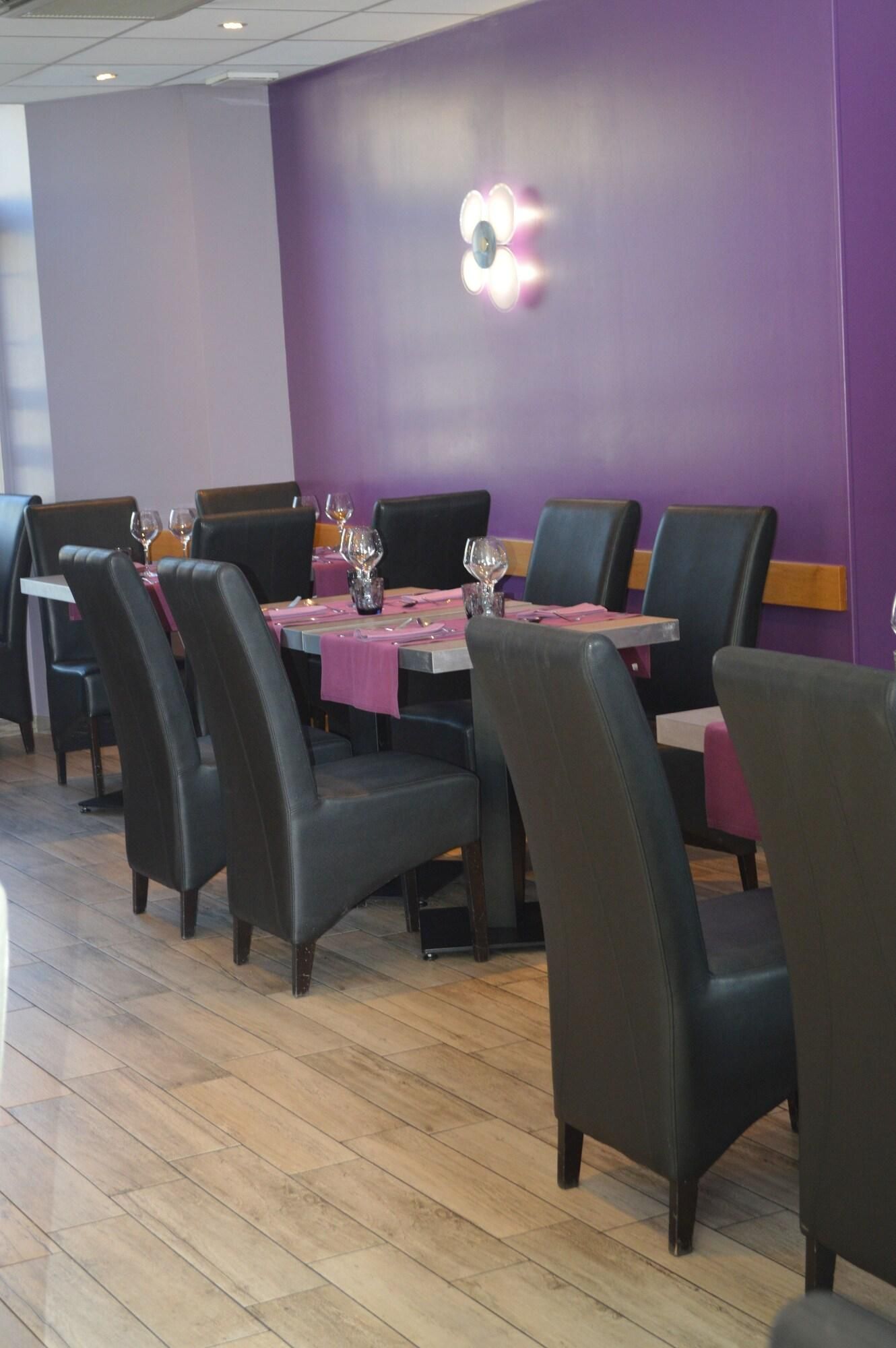 Un restaurant aux murs violets, aux chaises noires et au plancher en bois.