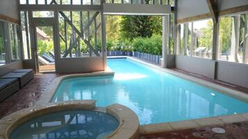 An indoor swimming pool with a hot tub, wooden deck, and glass doors.