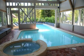 An indoor swimming pool with a hot tub, wooden deck, and glass doors. - Hôtel Le Grand Cerf (Lyons-la-Foret)