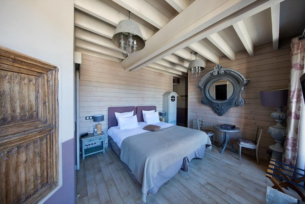 A bedroom with a wooden ceiling, a bed with a headboard, a nightstand, a mirror, and a small table with a chair.