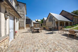 A courtyard with stone paving, outdoor seating, and traditional half-timbered buildings. - Hôtel Le Grand Cerf (Lyons-la-Foret)
