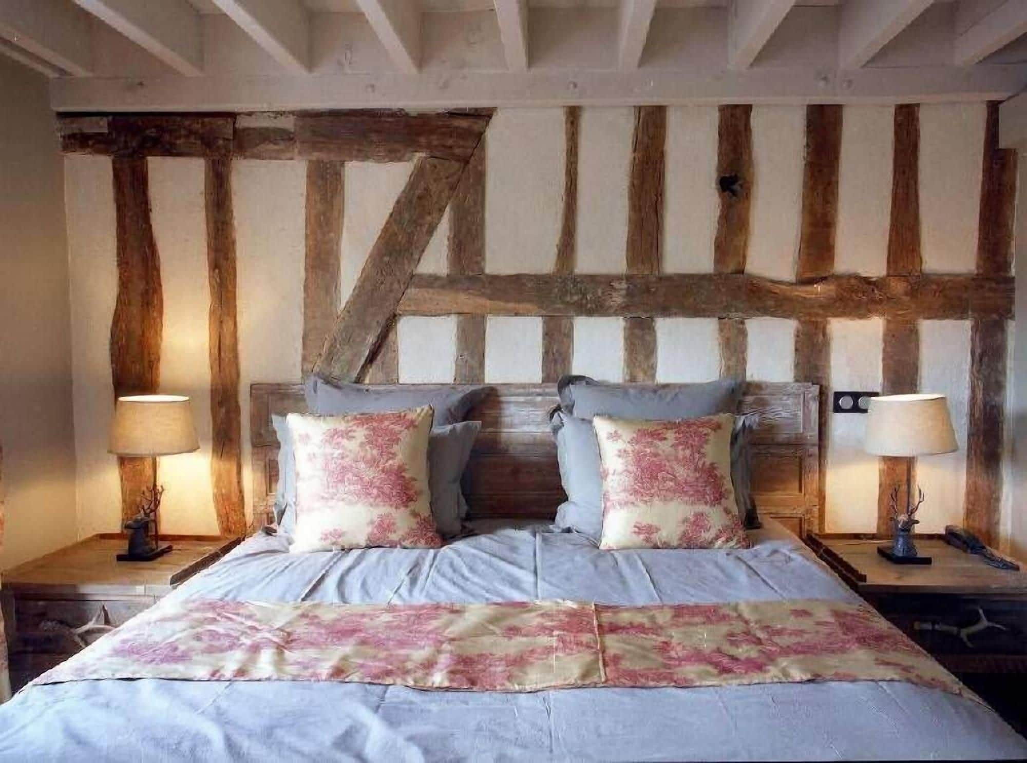 A bedroom with exposed wooden beams, a bed with floral bedding, and two bedside lamps.