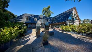 A courtyard with a stone archway, a building with a steep roof, and a paved walkway.