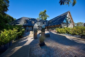 A courtyard with a stone archway, a building with a steep roof, and a paved walkway. - Hôtel Le Grand Cerf (Lyons-la-Foret)
