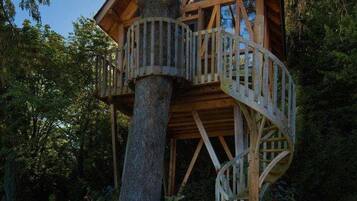 Uma casa na árvore com escada em espiral, rodeada por vegetação exuberante.