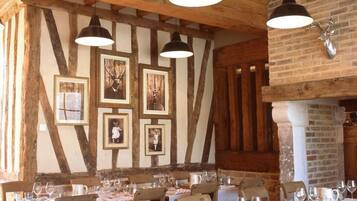 A dining area with wooden beams, framed pictures on the wall, and tables set for a meal.