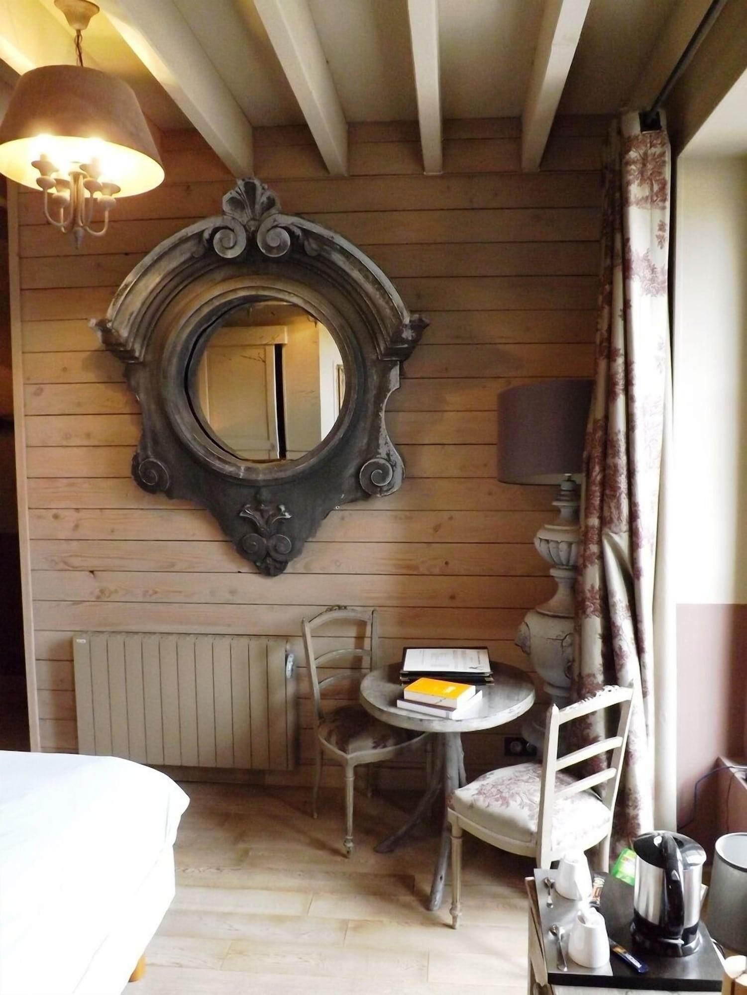 A room with a wooden ceiling, a round mirror, a table with a chair, a radiator, and a bed.