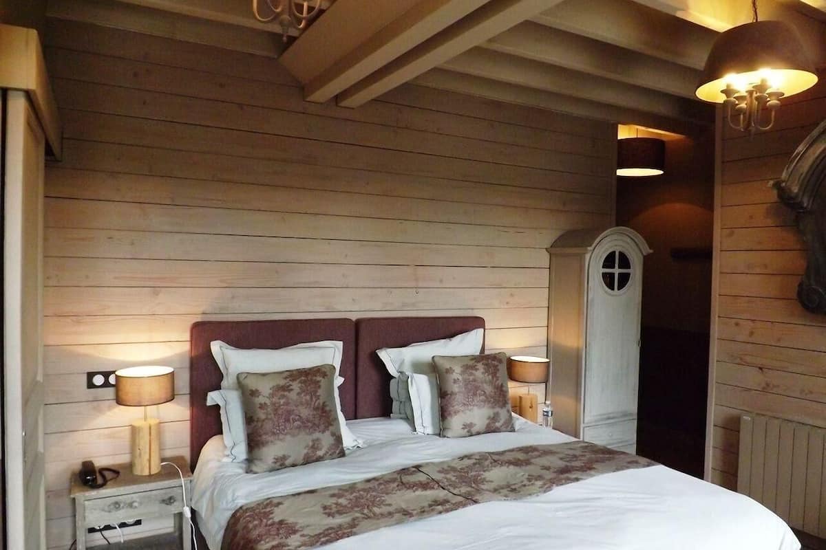 A wooden-paneled bedroom with a double bed, two bedside lamps, a nightstand, and a white arched door.