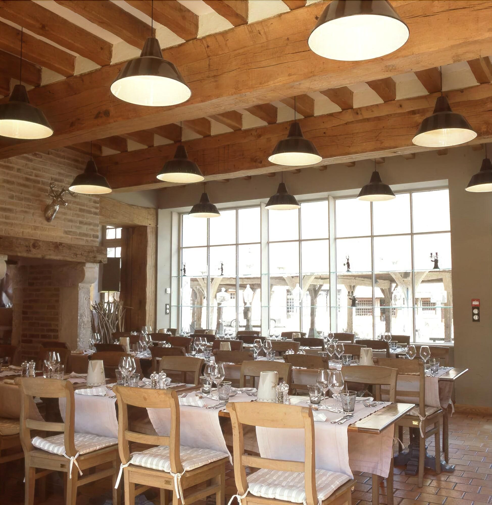 A restaurant with wooden beams, large windows, and tables set for dining.