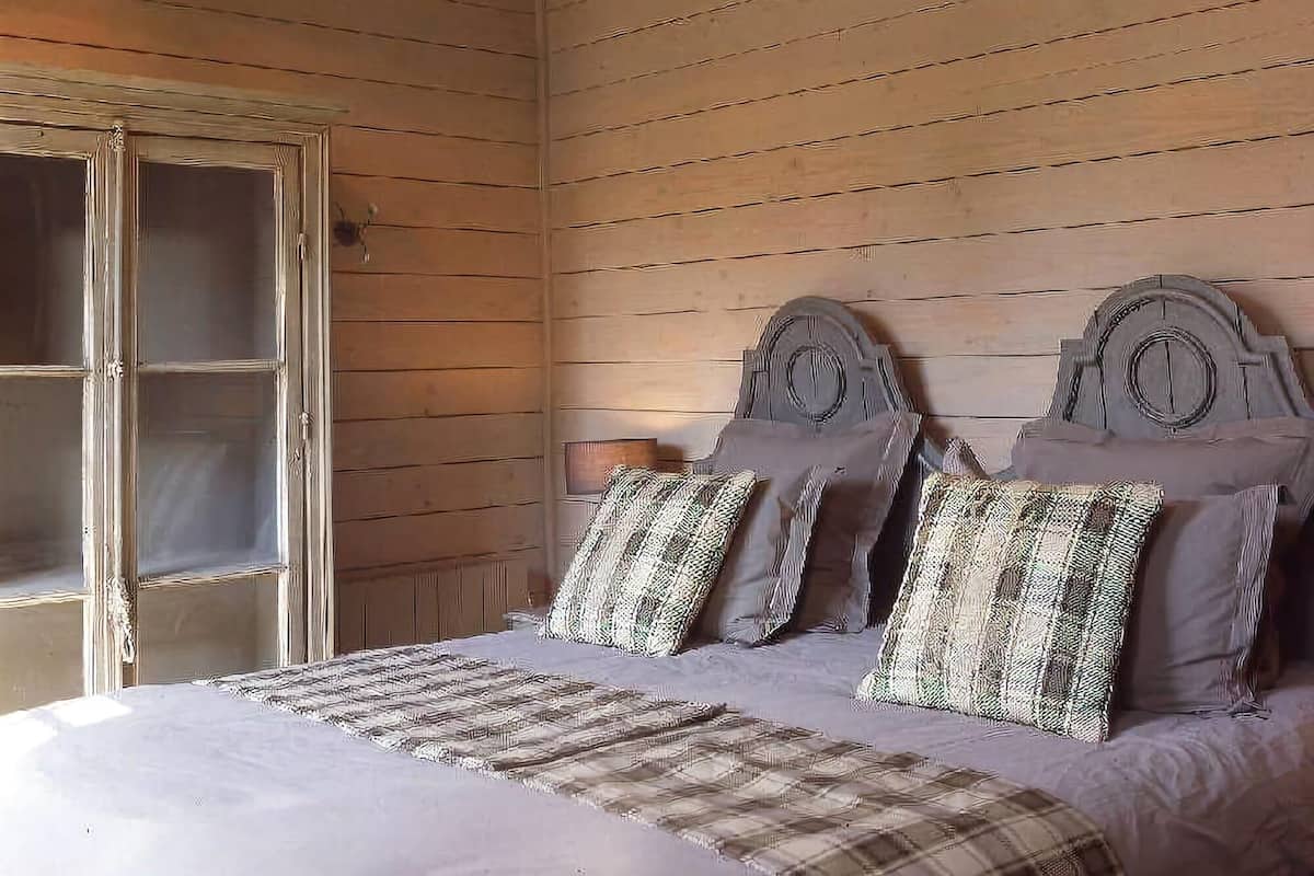 A wooden room with a bed, a chandelier, and a window with curtains.