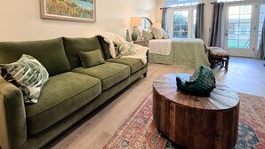 Una sala de estar con un sofá verde, una mesa de centro de madera y un cuadro en la pared.