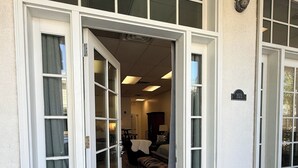 Fachada de un edificio con un par de puertas dobles, un espacio interior visible con comedor, y un cartel con el número de la dirección.