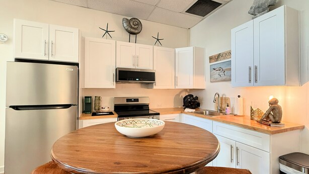 Una cocina moderna con armarios blancos, un refrigerador de acero inoxidable, un microondas y una mesa redonda de madera con taburetes.