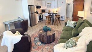 Una sala moderna con un sofá verde, un sillón marrón, una mesita de centro y una cocina al fondo.