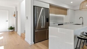 Une cuisine moderne dotée d’un réfrigérateur en acier inoxydable, de meubles blancs et d’un grand îlot central avec un évier.