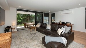Un salon moderne avec un canapé en cuir, une table basse en bois et une grande porte-fenêtre coulissante donnant sur un jardin.