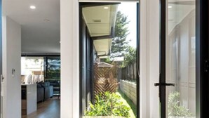 Un intérieur moderne avec un banc en bois, une statue de Bouddha et une vue sur un jardin, visible à travers une porte vitrée.