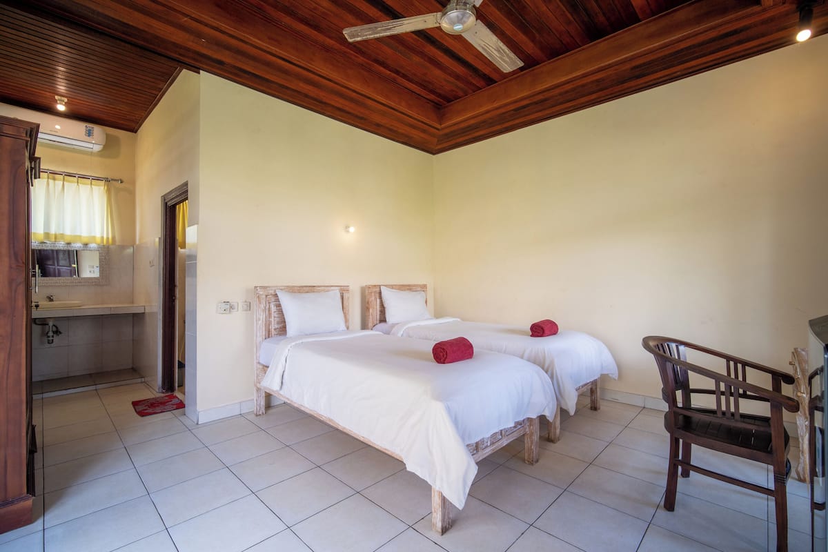 A room with two beds, a wooden ceiling, a small desk, and a chair.