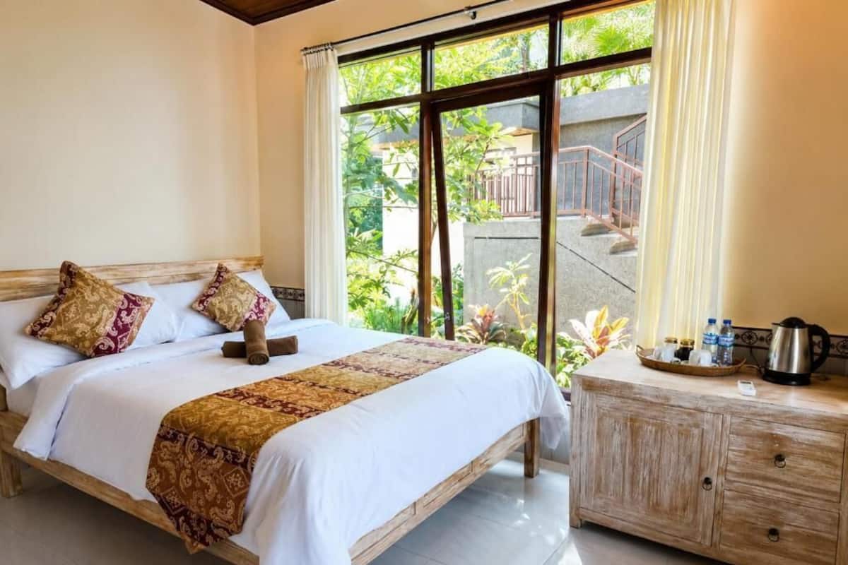 A bed with a patterned bedspread, a wooden headboard, and a nightstand with a kettle and bottles.