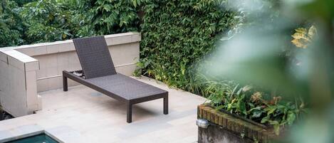 A poolside area with a lounge chair, a tiled deck, and a water feature.