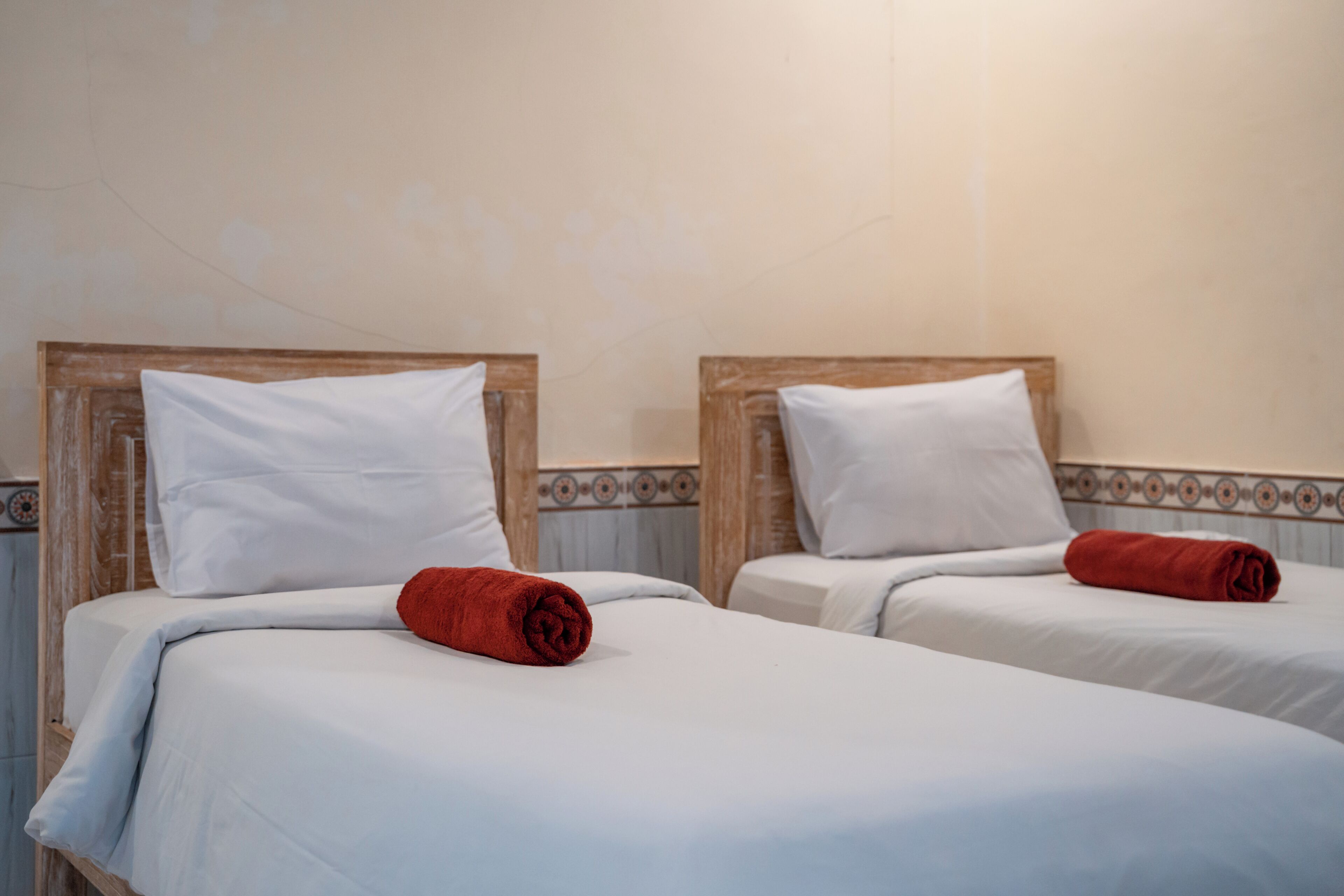 Two twin beds with white linens and red towels, wooden headboards, and a tiled border on the wall.