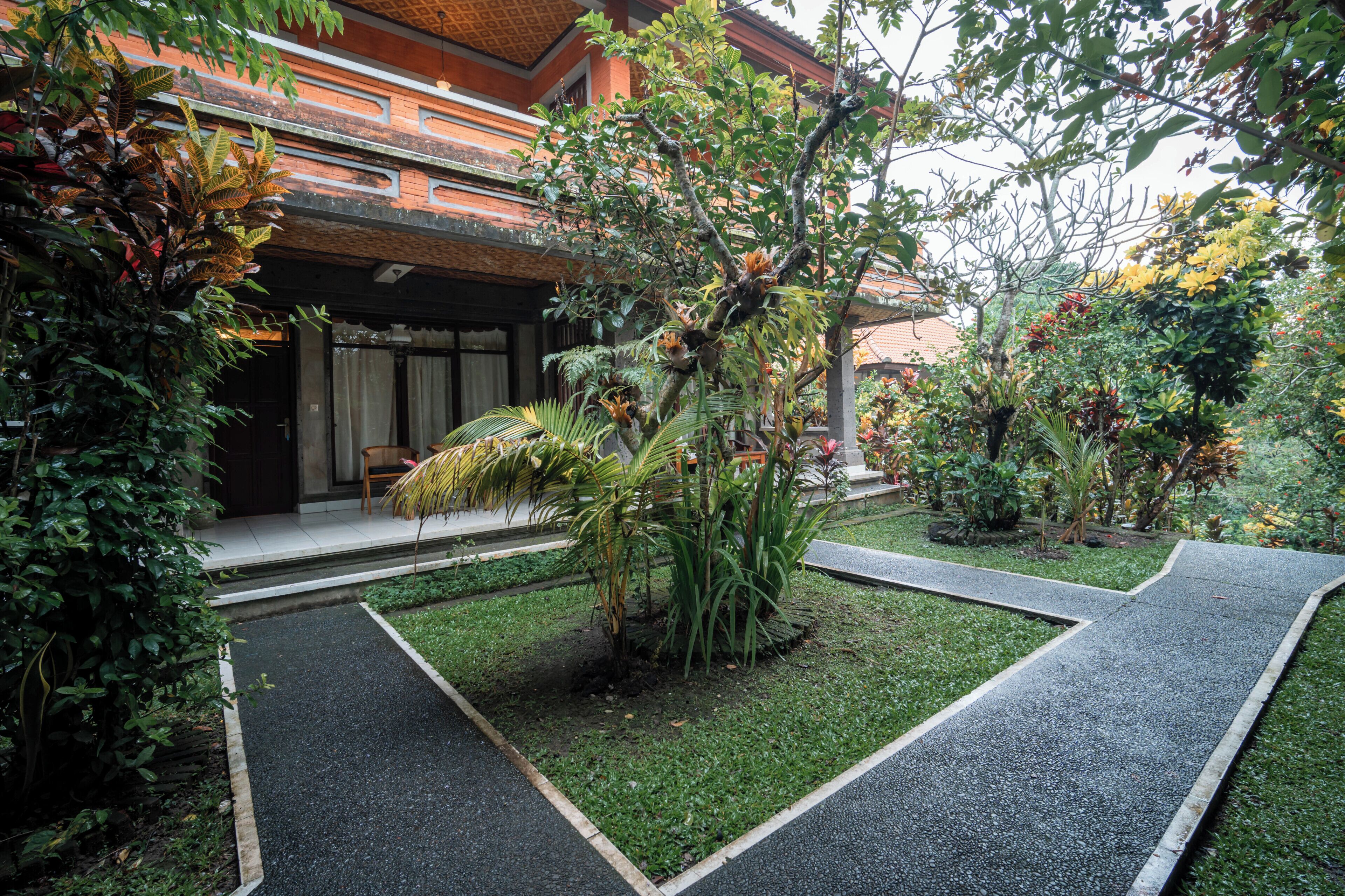 Un jardín con un sendero pavimentado, varias plantas y un edificio con techo de tejas.