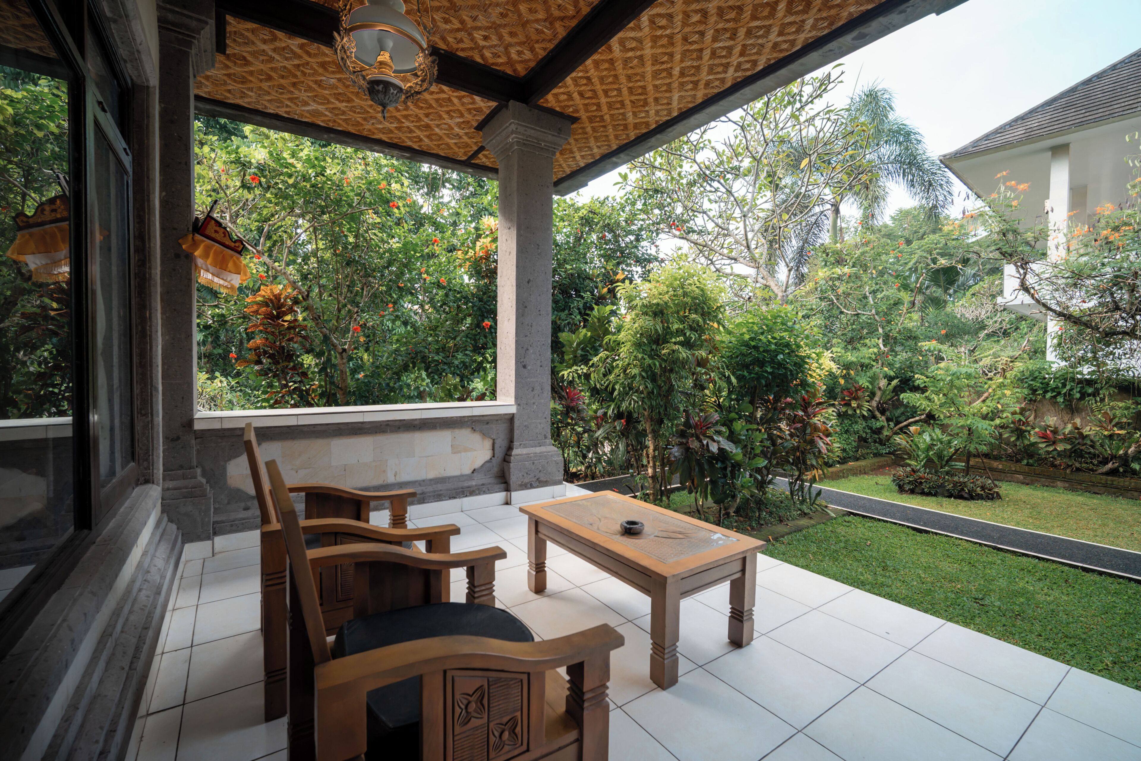 A covered patio with a table and chairs, a view of a garden with various plants and a pathway.