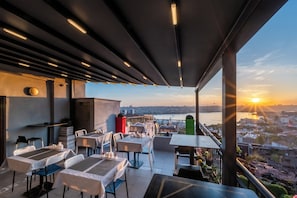 An outdoor terrace with tables and chairs, overlooking a cityscape and a body of water during sunset. - Taksim Terrapia Hotel (Istanbul)