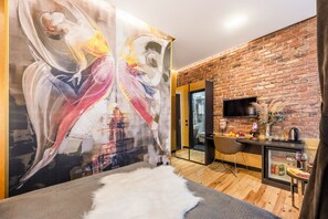 A modern room with a large abstract painting, a brick wall, a flat-screen TV, and a small kitchenette. - Taksim Terrapia Hotel (Istanbul)