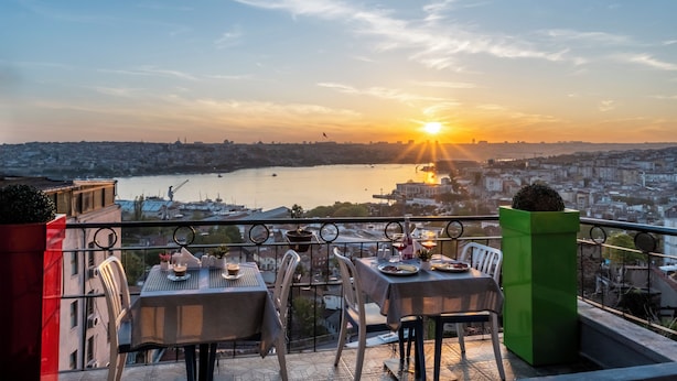 A terrace with tables and chairs overlooking a cityscape and a body of water during sunset. - Taksim Terrapia Hotel (Istanbul)