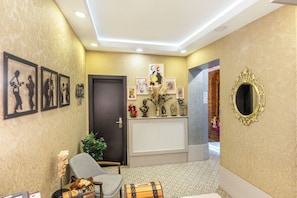 A reception area with a patterned wall, framed artwork, a decorative mirror, and a seating area with a chair and a small table. - Taksim Terrapia Hotel (Istanbul)