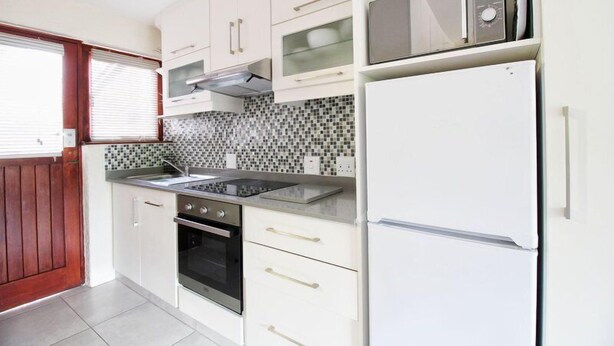 A kitchen with white cabinets, a black stove, a microwave, and a refrigerator. - Top Destinations (Southbroom)