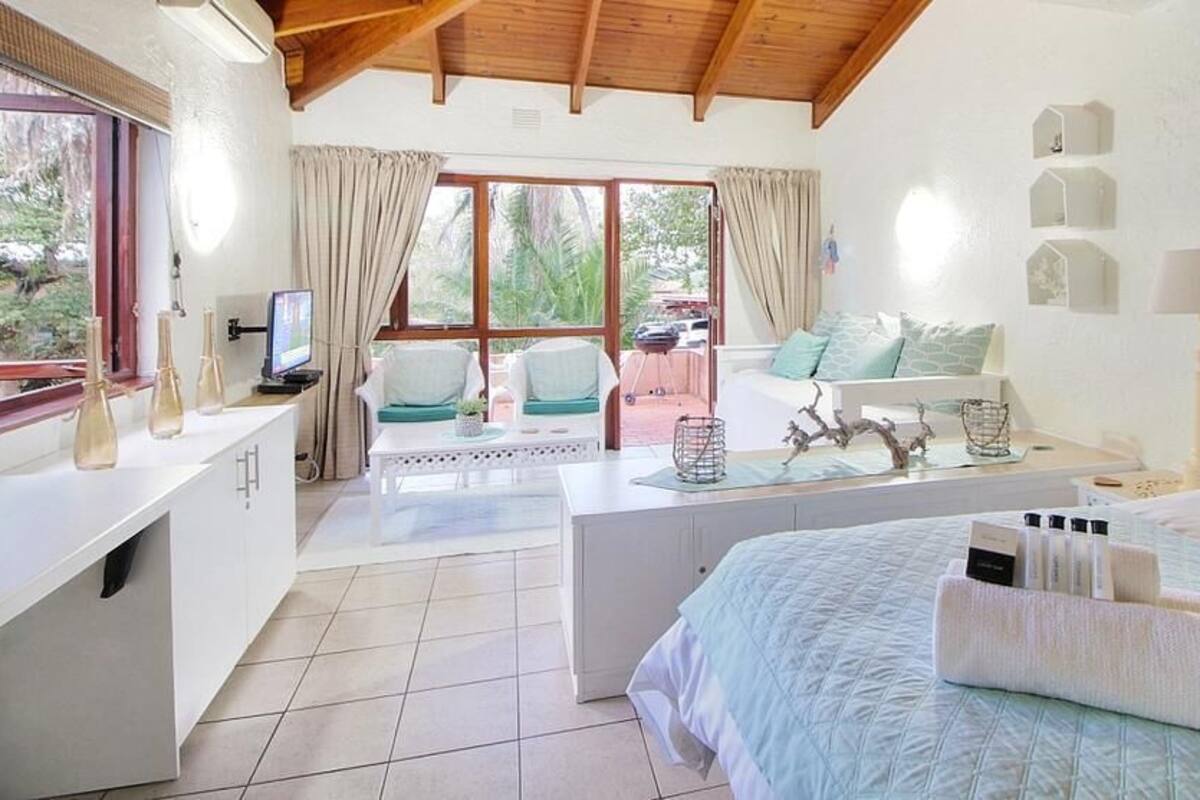 Une chambre à coucher avec un lit, des tables de chevet, un bureau, une chaise et une fenêtre avec des rideaux.