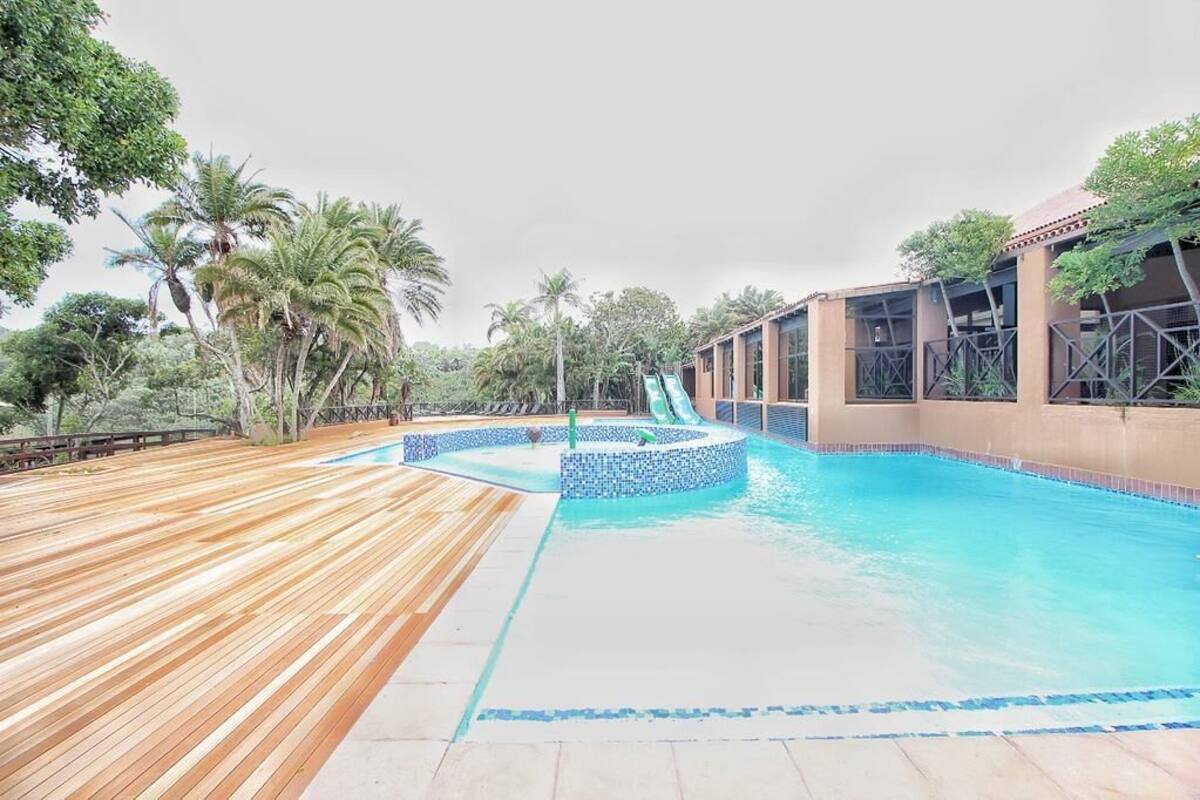 Un espace piscine doté d’une terrasse en bois, d’un toboggan et d’un bâtiment aux grandes fenêtres.